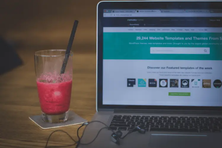 notebook com site aberto sobre a mesa ao lado de um copo de suco